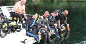 scuba training - 5 participants sitting on a dock in wetsuits preparing to scuba dive